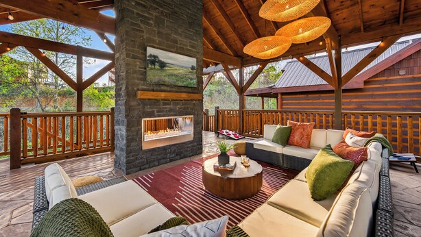 A covered outdoor seating area with a fireplace, wooden furniture, and a view of the outdoors. - Bethlehem Lodge (Sevierville)