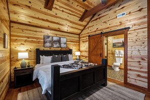 A wooden cabin bedroom with a bed, nightstands, a sliding door, and a view of the outside. - Bethlehem Lodge (Sevierville)