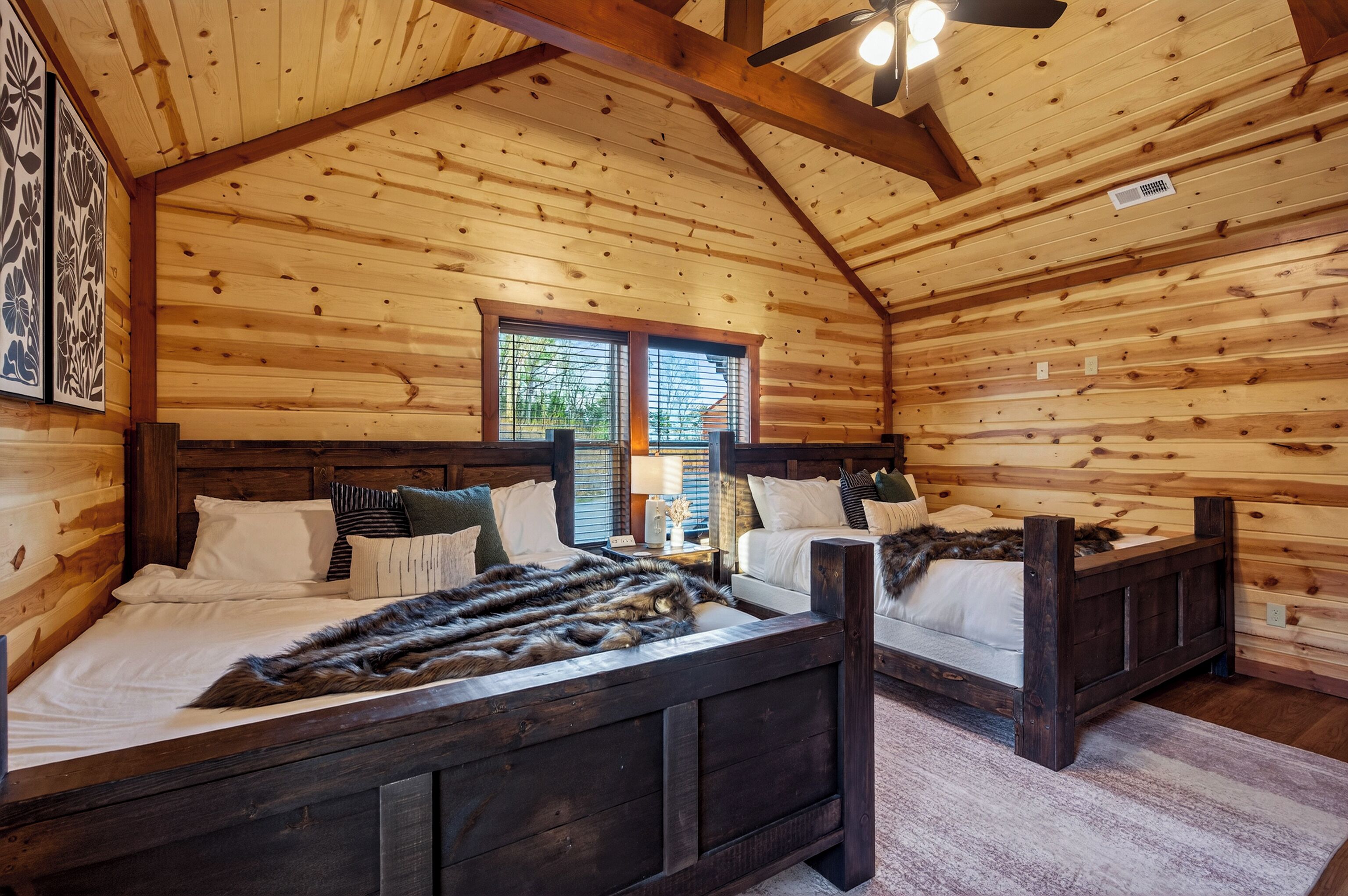 Ein Schlafzimmer einer Holzhütte mit zwei Betten, einem Deckenventilator und einem Fenster mit Jalousien.