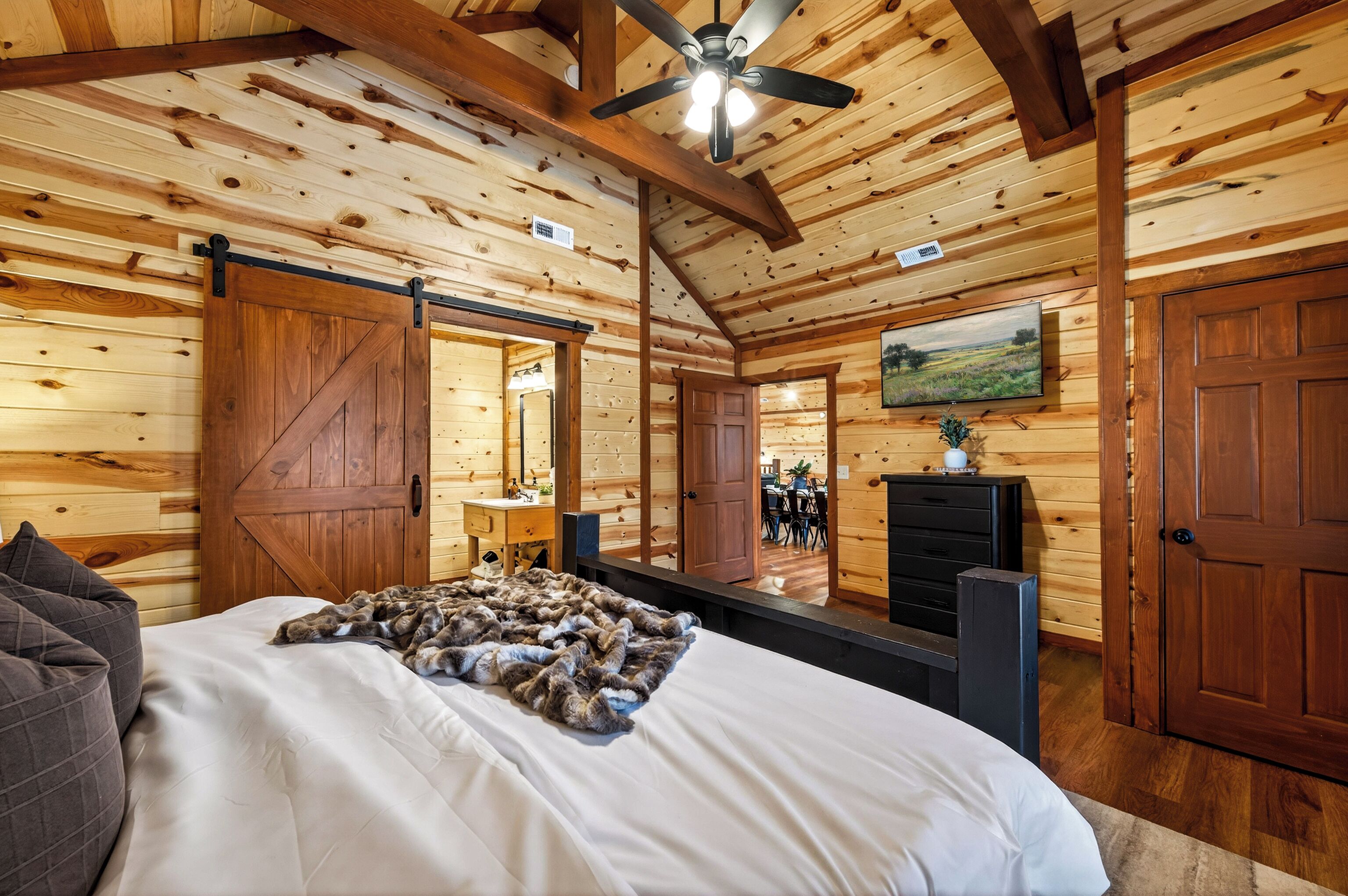Une chambre à coucher avec un lit, un ventilateur de plafond, des murs en bois, un grand miroir et un téléviseur.