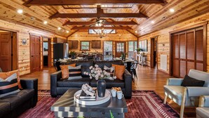 A spacious log cabin interior with a central seating area, kitchen, dining space, and large windows. - Bethlehem Lodge (Sevierville)