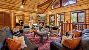 A log cabin interior with a fireplace, seating area, and large windows. - Bethlehem Lodge (Sevierville)
