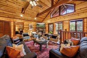 A log cabin interior with a fireplace, seating area, and large windows. - Bethlehem Lodge (Sevierville)