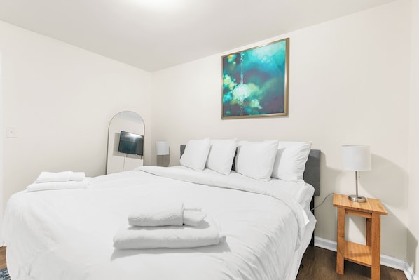 A hotel room with a large bed, a bedside table with a lamp, a wall-mounted TV, and a painting above the bed.