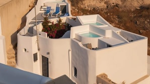 A white building with a rooftop pool, lounge chairs, and a small garden area. - Fira Home With Rooftop Hot Tub (Santorini)
