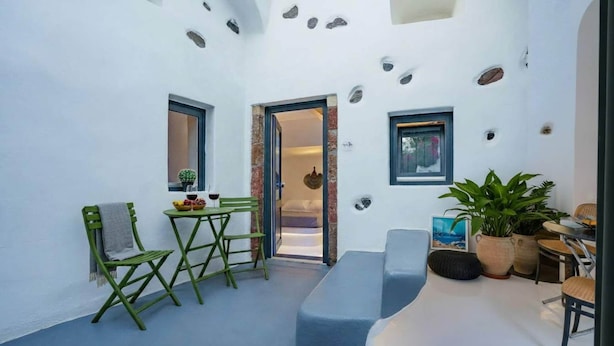 A small, open-plan living space with a dining area, seating, and a view into the bedroom. - Fira Home With Rooftop Hot Tub (Santorini)