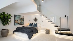 Ein modernes Schlafzimmer mit Bett, Nachttisch, Lampe und einer großen Topfpflanze.