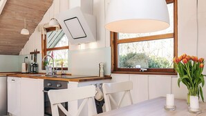 A modern kitchen with wooden beams, a large window, and a dining area with a white table and chairs. - 4 Person Holiday Home in Gilleleje (Gilleleje)