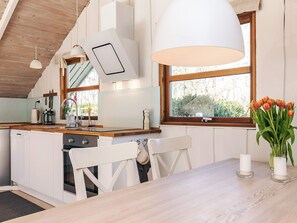 Eine moderne Küche mit Holzbalken, einem großen Fenster und einem Essbereich mit weißem Tisch und Stühlen.