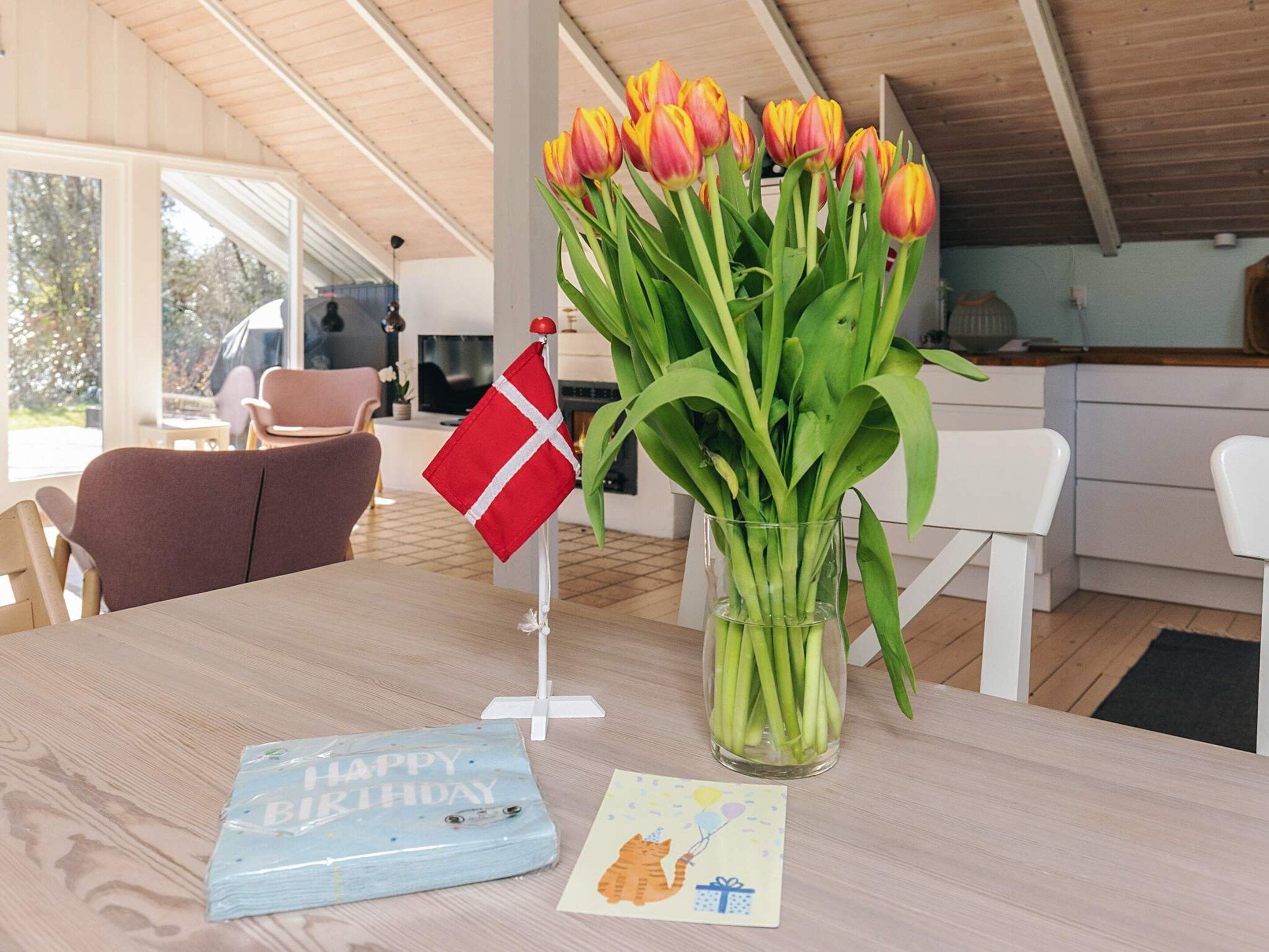 A dining table with a glass vase of tulips, a Danish flag, a birthday card, and a small gift box.