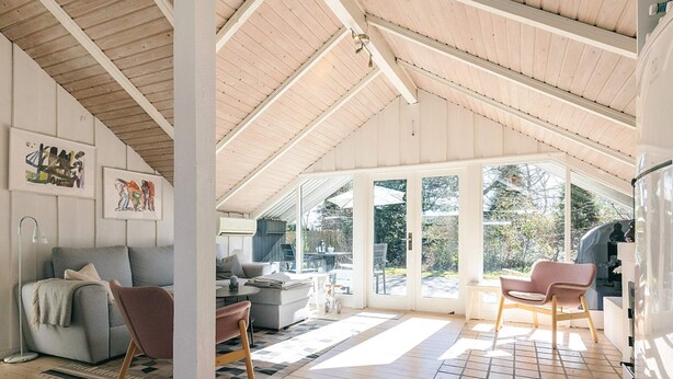 A spacious room with a high ceiling, wooden beams, a large sliding glass door, a sofa, a chair, and a dining table. - 4 Person Holiday Home in Gilleleje (Gilleleje)