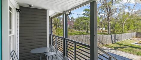 A covered porch with a table and chairs, a view of the backyard, and a wooden fence.