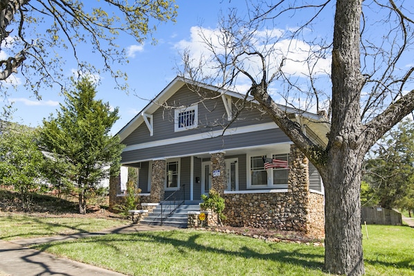 A two-story house with a stone foundation, a front porch, and a flag.