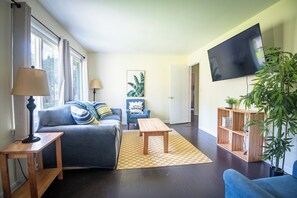 A living room with a sofa, a coffee table, a TV, and a bookshelf. - The Garden Park Escape: Pool/Patio/Groups/King Bed (Birmingham)