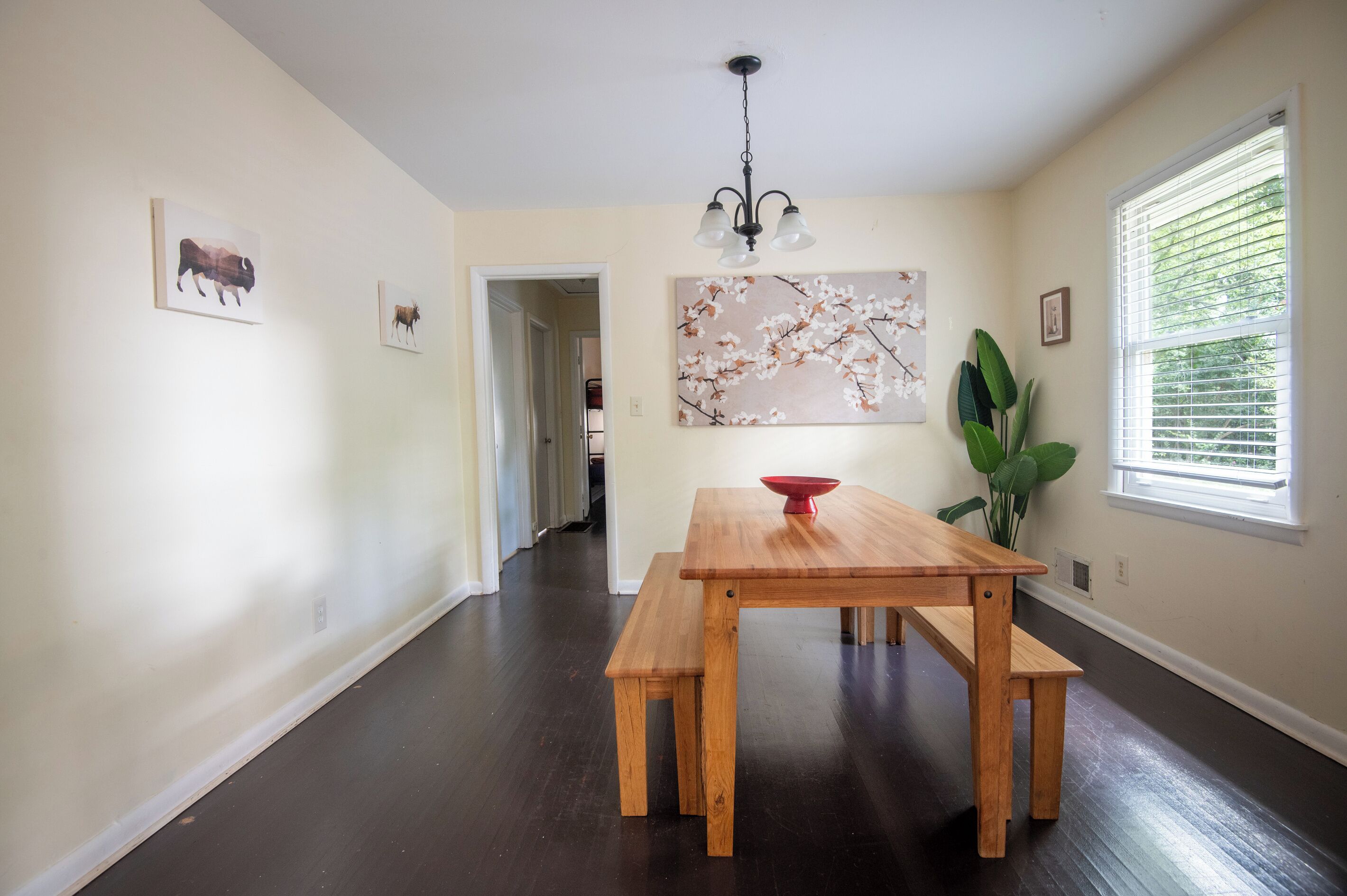 A dining area with a wooden table and benches, a chandelier, and artwork on the walls.