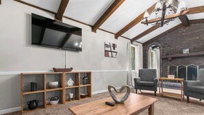 A living room with a TV, wooden shelves, a fireplace, and two armchairs. - The Poolside Haven | Family/Backyard/Game Room Fun (Birmingham)