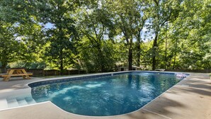 A swimming pool with a curved edge, surrounded by a concrete deck and trees. - The Poolside Haven | Family/Backyard/Game Room Fun (Birmingham)