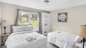 A bedroom with two beds, a window with curtains, a bookshelf, and a flower painting. - The Poolside Haven | Family/Backyard/Game Room Fun (Birmingham)
