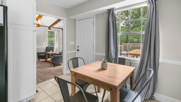 A dining area with a wooden table and chairs, a potted plant, and a view of a deck through a window. - The Poolside Haven | Family/Backyard/Game Room Fun (Birmingham)