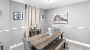 A dining area with a wooden table, chairs, a bench, a candle holder, and two framed pictures on the wall.