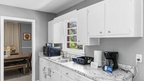 A kitchen with white cabinets, a granite countertop, a microwave, a coffee maker, and a window with a view of trees.