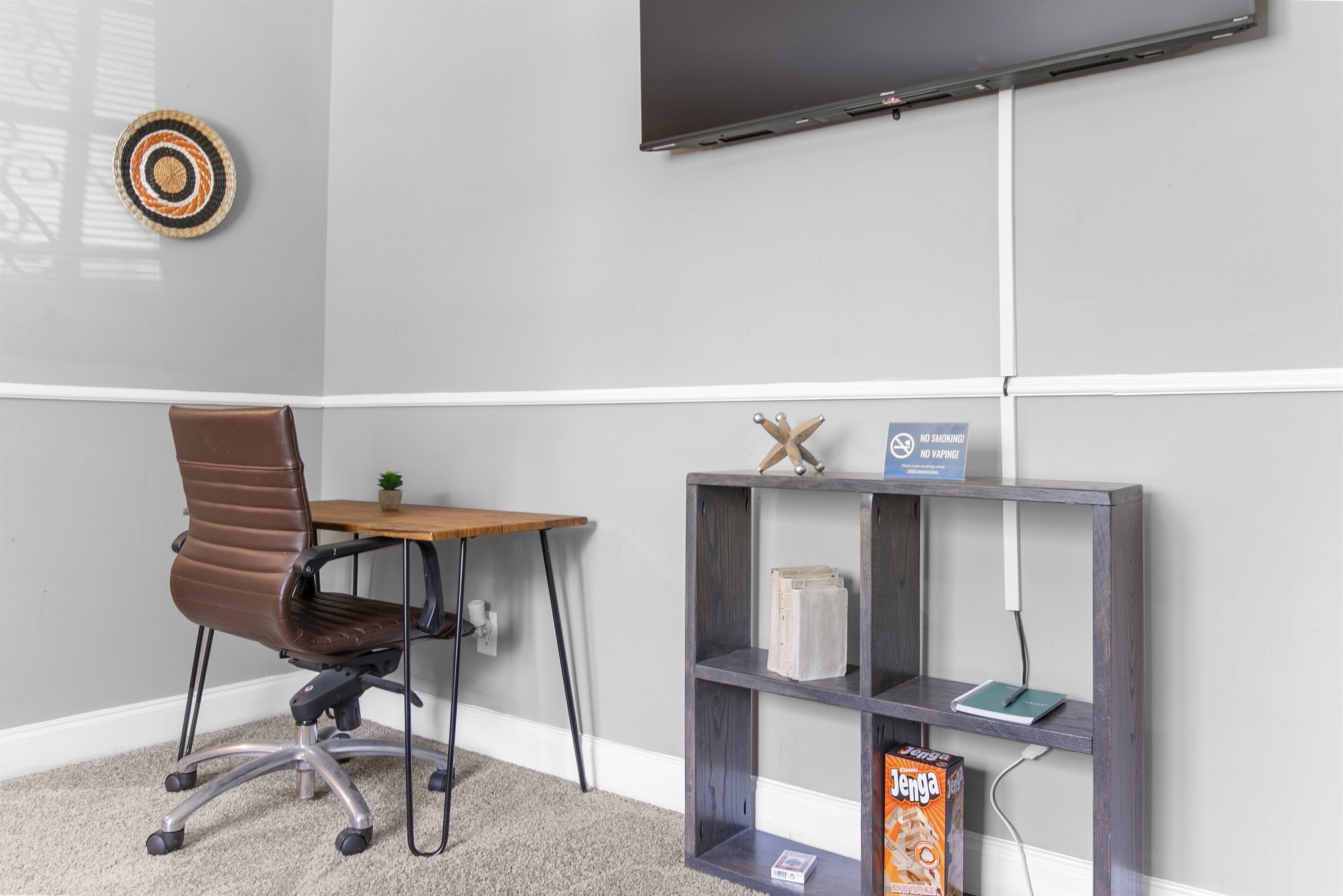A room with a desk, chair, TV, shelf, and a no smoking sign.