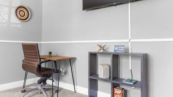 A room with a desk, chair, TV, shelf, and a no smoking sign.