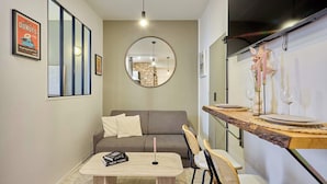 A compact living space with a sofa, a dining table with chairs, a mirror, and a wall-mounted TV. - Charming Apartment - Paris Pere Lachaise (Paris)