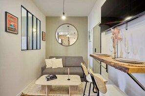 Ein kompakter Wohnbereich mit Sofa, Esstisch und Stühlen, einem Spiegel und einem an der Wand befestigten Fernseher.