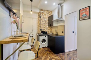 Eine kompakte Küche mit Backsteinwand, einer Waschmaschine und einem Essbereich mit Holztisch und Stühlen.