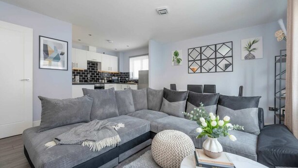 A modern living room with a grey sofa, a coffee table, and a kitchen in the background. - London Flat With Private Entrance (London)