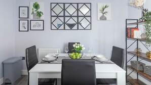 A dining room with a white table, black chairs, a vase of flowers, and framed artwork on the wall. - London Flat With Private Entrance (London)