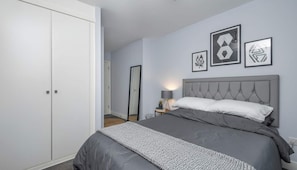 Ein Schlafzimmer mit einem Bett, einem Nachttisch, einer Lampe und gerahmten Kunstwerken an der Wand.