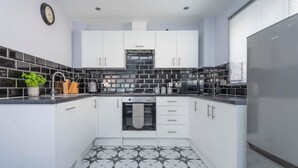 A modern kitchen with white cabinets, black and white tiles, a built-in oven, and a clock on the wall. - London Flat With Private Entrance (London)
