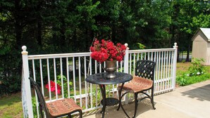 A patio with a round table and two chairs, a white fence, and a shed in the background.