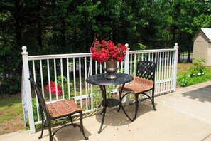 A patio with a round table and two chairs, a white fence, and a shed in the background.