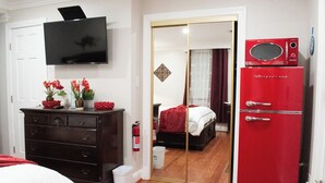 A bedroom with a TV, dresser, red refrigerator, and a mirror reflecting the room.