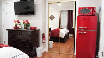 Une chambre avec une télévision, une commode, un réfrigérateur rouge et un miroir qui reflète la pièce.