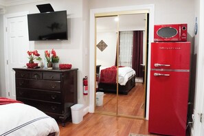 A bedroom with a TV, dresser, red refrigerator, and a mirror reflecting the room.