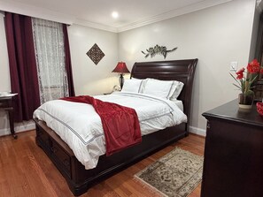 A neatly made bed with a red blanket, a bedside table with a lamp, and a decorative wall piece. - Private Suite 3 near National Harbor Pvt Entry (Fort Washington)