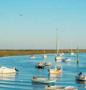 A calm water body with several boats anchored, a clear sky, and a distant shoreline. - O Lagar Apartamento T1 a 200m Campo Golfe (Conceição de Tavira)