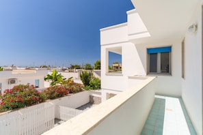 Ein modernes Gebäude mit weißer Fassade, einem Balkon mit weißer Brüstung und Blick auf die Umgebung.
