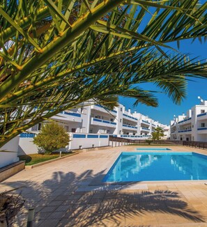 Ein Swimmingpool, umgeben von Palmen und weißen Gebäuden mit blauen Akzenten.