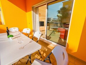 A dining area with a table, chairs, a wine bottle, and a small plant. - Royal Cabanas Golf Apartamento T3 (Conceição de Tavira)