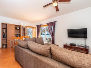 Una sala de estar con sofá, televisor, ventilador de techo y un comedor con sillas y mesa.