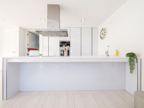 A modern kitchen with white cabinetry, a stainless steel range hood, a clock, and a small plant on the counter. - V3 Moradia Golden Nelly com piscina (Luz de Tavira)