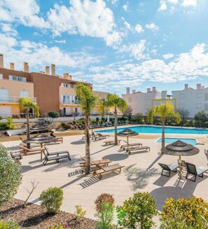 A poolside area with lounge chairs, umbrellas, and a swimming pool.