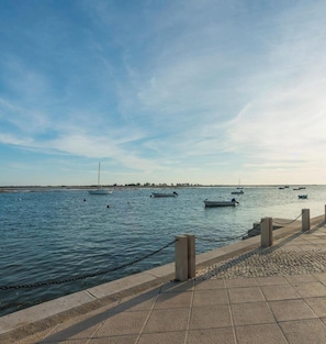 A waterfront promenade with a clear sky, calm water, and several boats. - Casa Buganvília – Casa citadina T1 Centro Cidade. (Tavira)