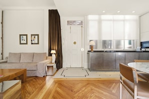 A modern living room with a sofa, a dining table, and a kitchen area with cabinets and a countertop. - 1905 Corner Flat · Temporary Stay · Las Letras (Madrid)