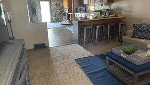 Eine moderne Küche mit einer zentralen Kochinsel, Barhocker und einer Essecke mit einer Couch und Kissen.
